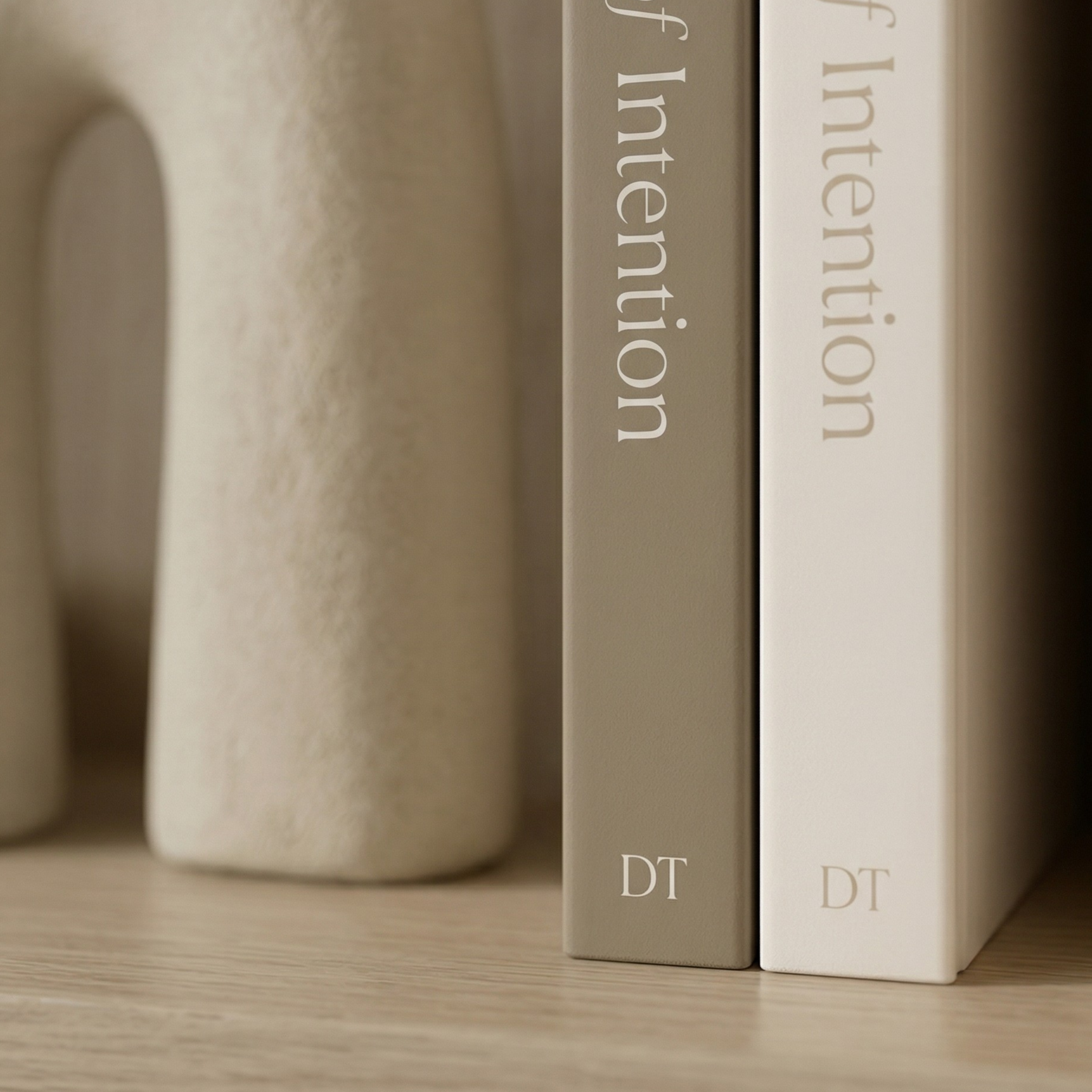 Two books titled 'The Architecture of Intention by DT Home on a wooden shelf with a ceramic vase side by side standing